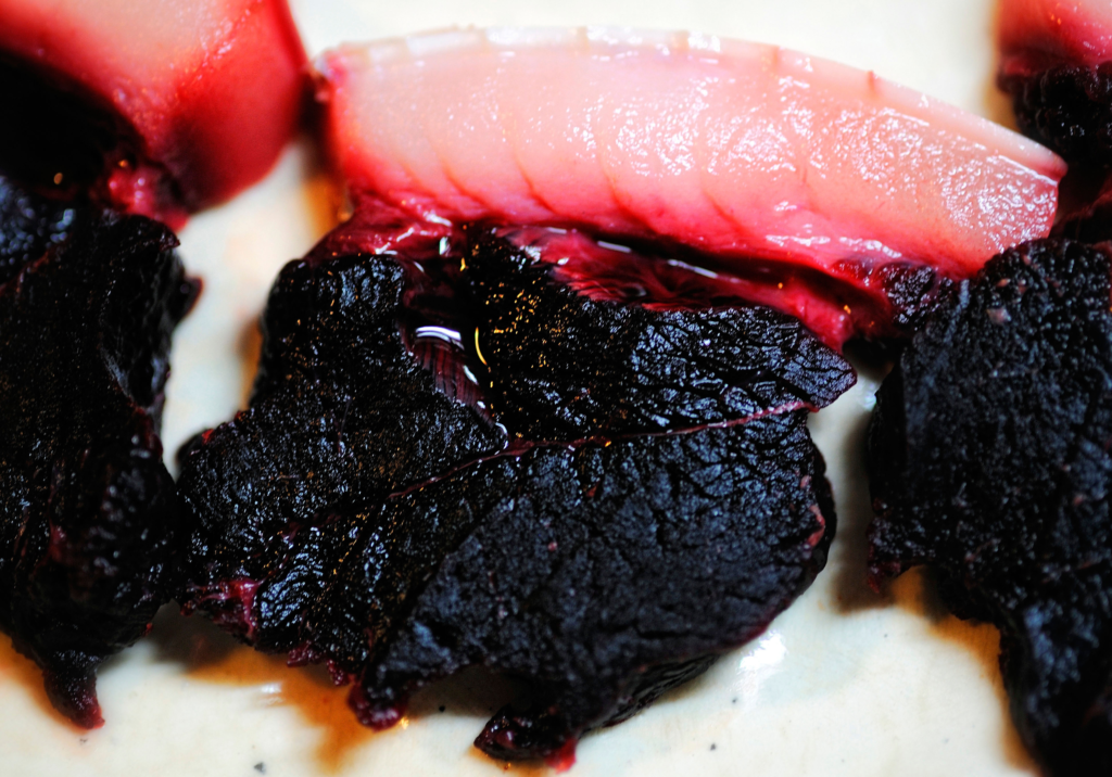 Close-up of sliced dolphin meat, showing a deep red and black coloration with visible fat layers. This meat is known to contain high levels of mercury and other toxins.