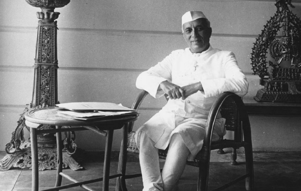  Jawaharlal Nehru seated in a chair in traditional Indian attire, posing in a relaxed and reflective manner, symbolizing his role as the first Prime Minister of independent India.