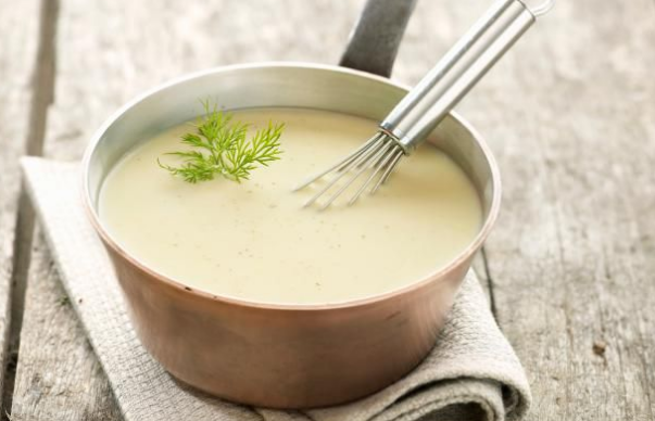 A smooth Velouté sauce in a copper pan with a whisk