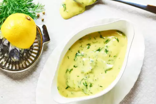 A bowl of Hollandaise sauce garnished with fresh dill and a lemon