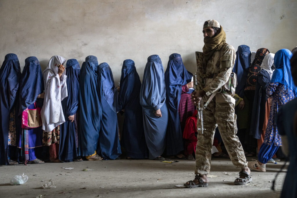 A Taliban fighter stands guard as women wait to receive food rations in Kabul, Afghanistan, on May 23, 2023.