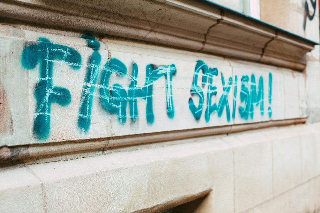 Graffiti with the words 'Fight Sexism!' spray-painted in blue on a beige wall, highlighting the message of gender equality and the ongoing trend of addressing sexism, inspired by the viral man vs. bear incident.