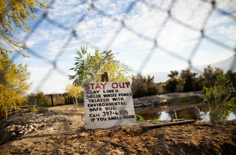 A hand-written sign warns Duroville mobile home park residents in Thermal, California, to stay away from a waste pond on the neighboring property.