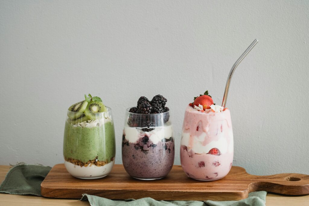 Assorted yoghurt parfaits in glasses, featuring layers of yoghurt, fruits, and granola.