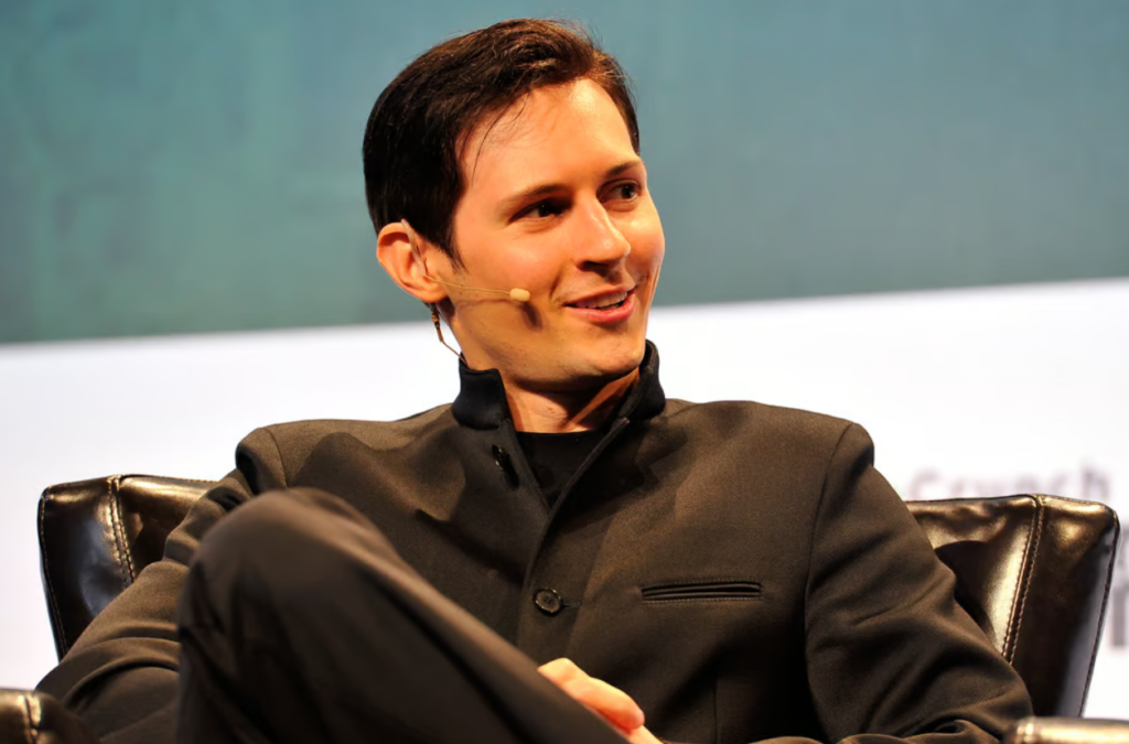 Photo of Pavel Durov, the founder of Telegram, sitting on a stage during an event, wearing a dark suit and smiling while speaking into a microphone headset