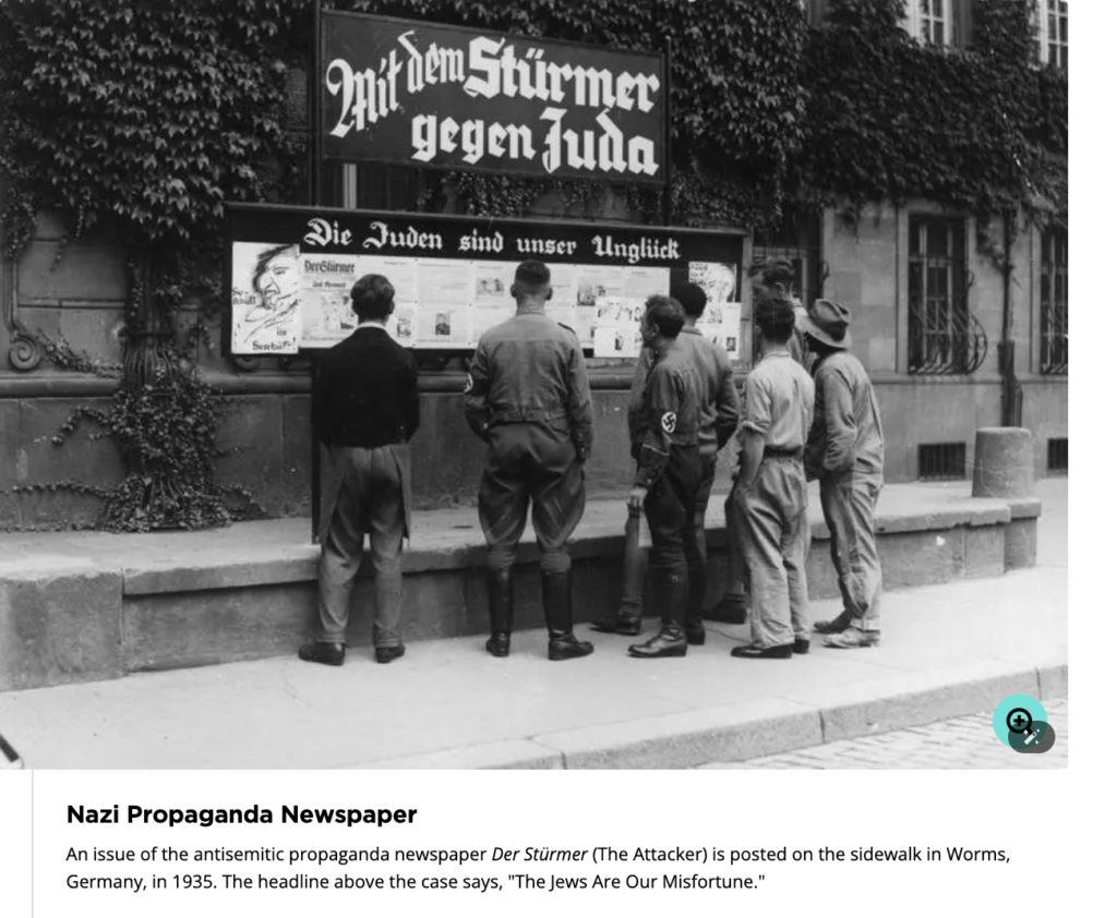 A group reading an anti-Semitic publication titled ‘Der Stürmer gegen Juda,’ exemplifying Nazi propaganda against Jewish people.